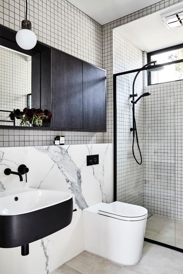 A contemporary bathroom featuring small white grid tiles with dark grout, a dramatic black timber vanity and round black basin, white marble-look wall panels with grey veining, and matte black tapware and shower framing. A frameless glass shower enclosure, wall-hung toilet, mirrored cabinet, pendant light, and high window complete the monochromatic scheme.