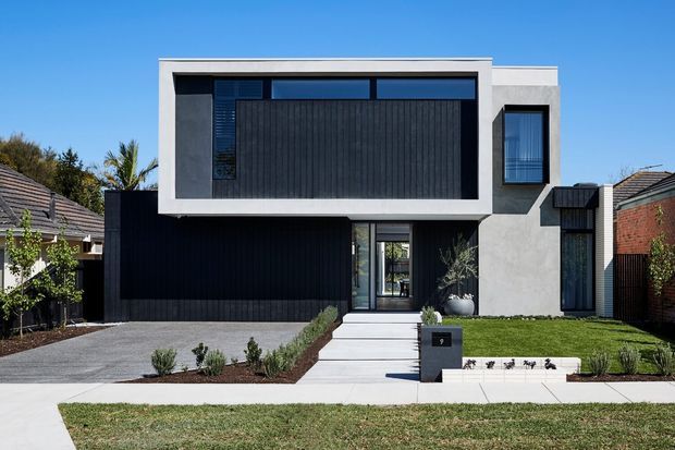 Front exterior view of a contemporary two-storey residence with a crisp white rendered facade, extensive dark vertical cladding, large horizontal upper-level glazing, a recessed entry, double garage, concrete driveway and minimalist landscaped frontage.