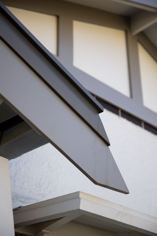 Close-up architectural detail of overlapping angular roof or canopy elements with dark trim, white painted surfaces, exposed beams, and strong geometric shadows. The image focuses on the building exterior rather than an occupied interior space.