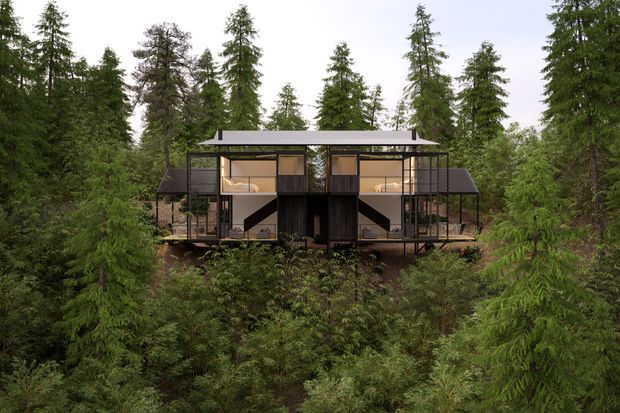 Front exterior view of a contemporary elevated house set within dense evergreen forest. The symmetrical timber-and-glass structure features dark cladding, extensive glazing, open balconies or decks, slender supports, and a broad low-pitched roof.