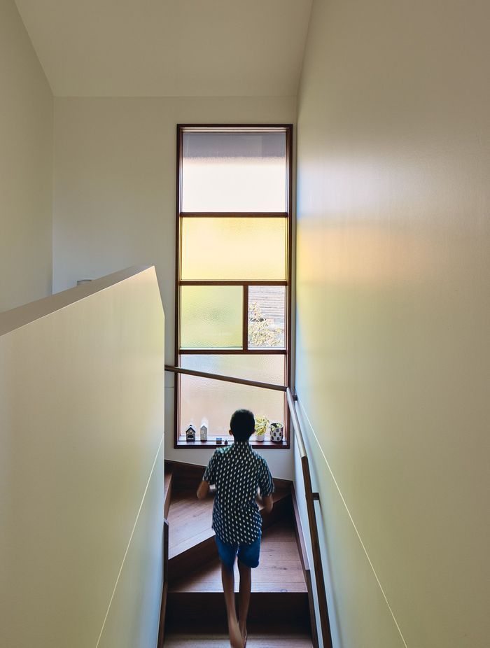 Coloured glass within the stairway and kitchen windows, along with a skylight shaft bathing the home’s entry in warm light, introduces zesty oranges, greens, reds and yellows into daily life.