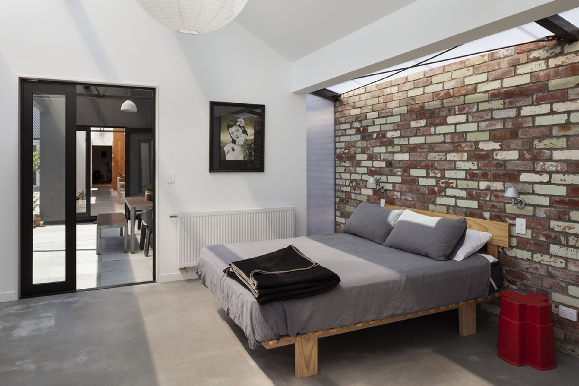 A long, narrow strip of polycarbonate roofing draws soft, diffused light into the bedroom, adding texture and interest to a recycled brick wall that runs the entire length of the new addition.