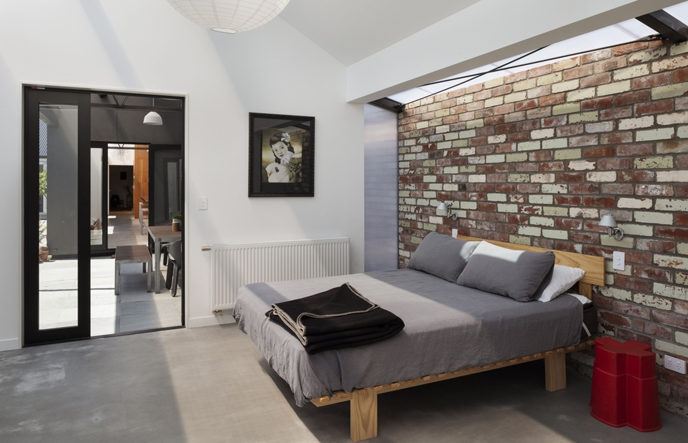 A long, narrow strip of polycarbonate roofing draws soft, diffused light into the bedroom, adding texture and interest to a recycled brick wall that runs the entire length of the new addition.