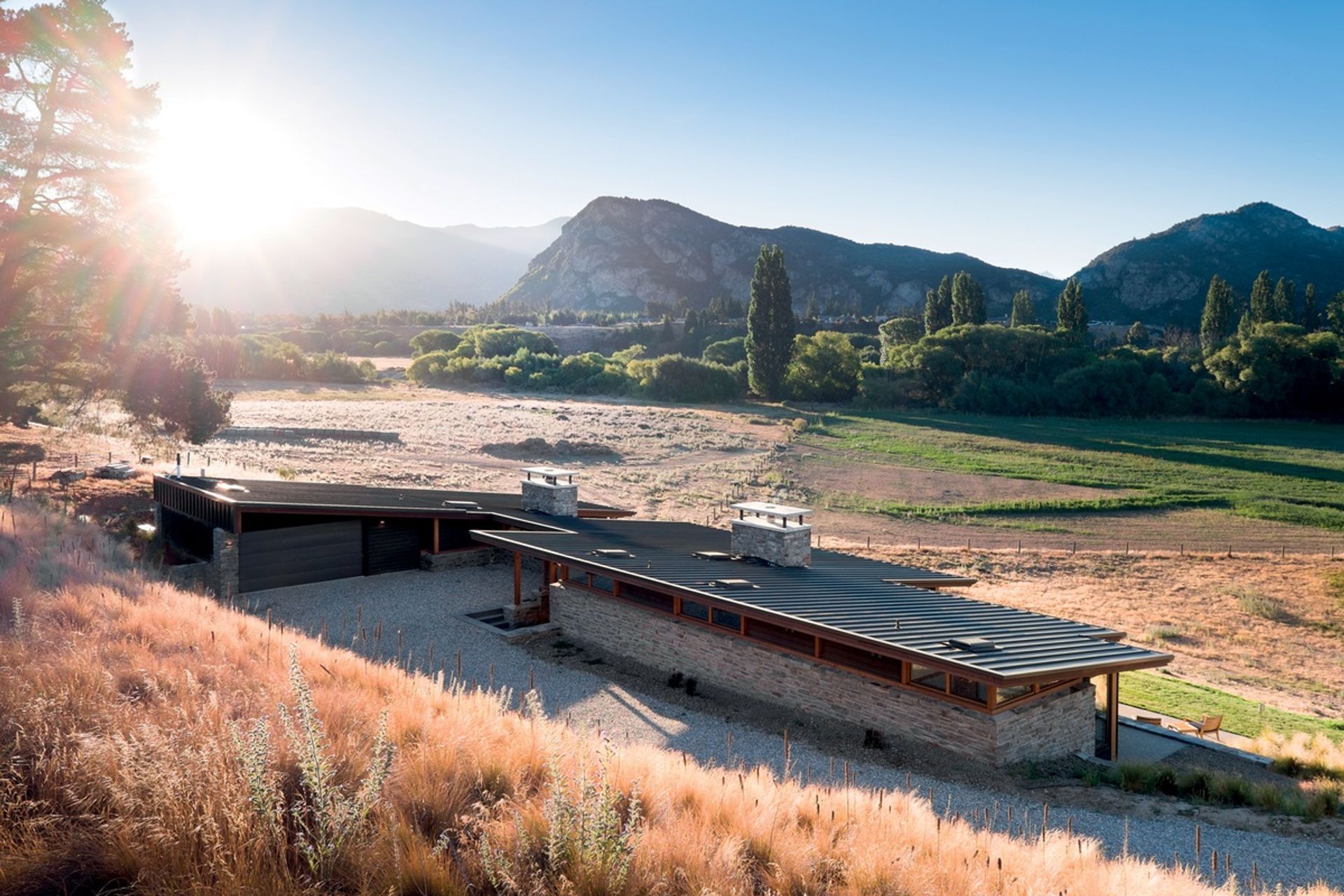 The distinctive sharp, sloping roof and two large schist chimneys of the Cardrona River House by Mason &amp; Wales Architects are great features of this impressive home. | Photography: Dennis Radermacher