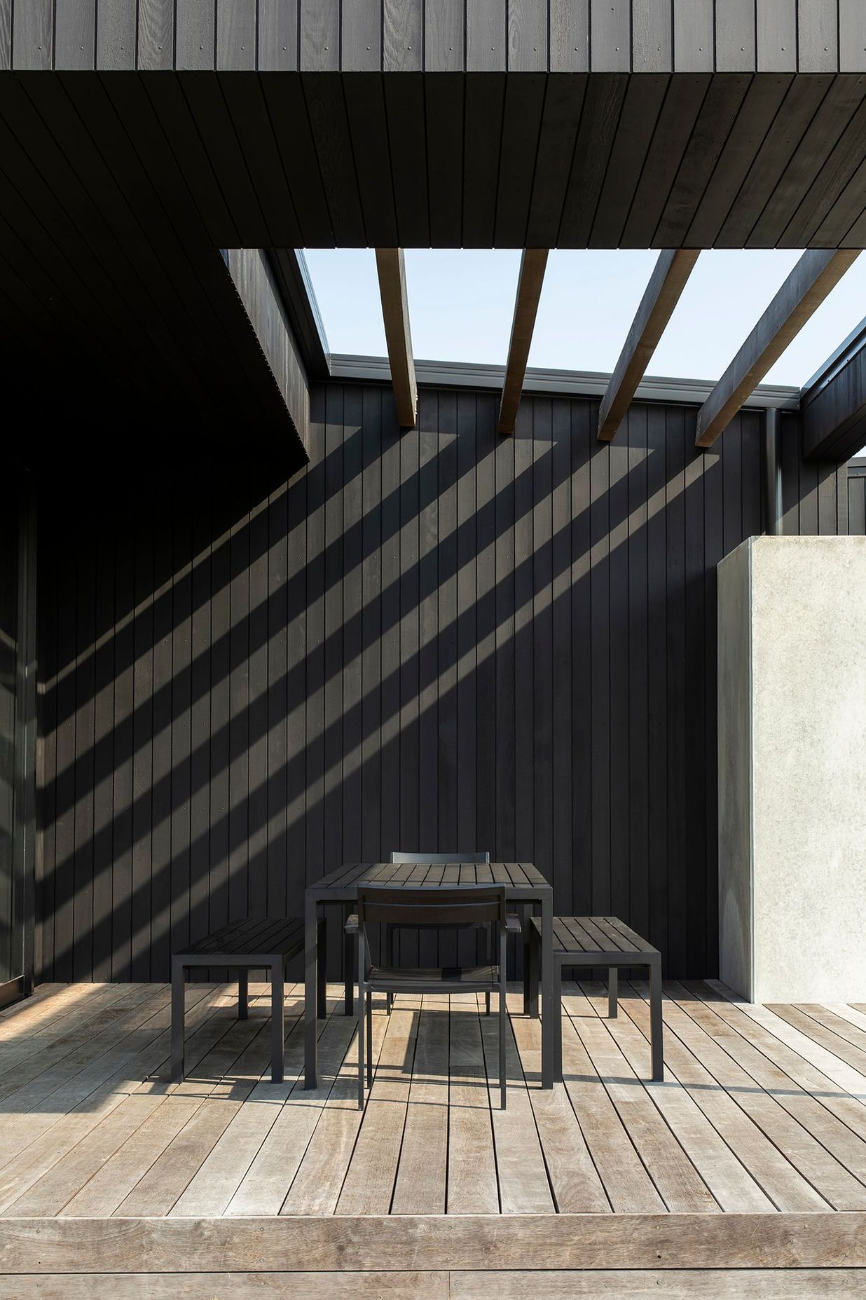 At Vineyard House, shadows from the overhead louvres stripe the timber wall of the outdoor room.