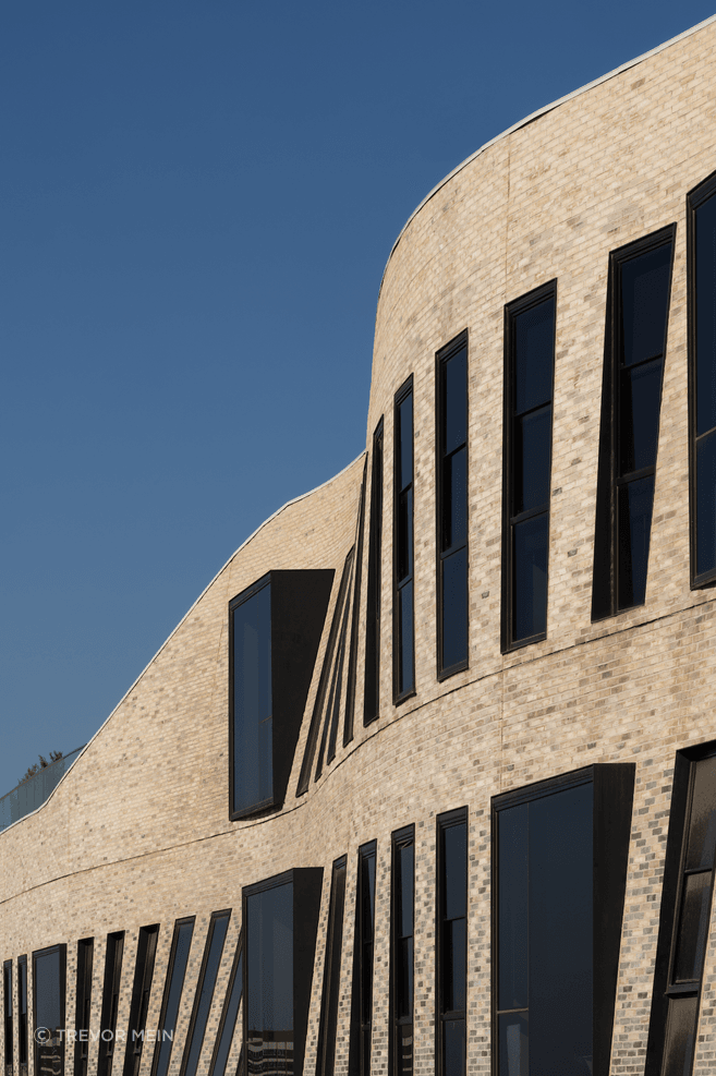 The textured façade of Petersen bricks forms a curved veil.