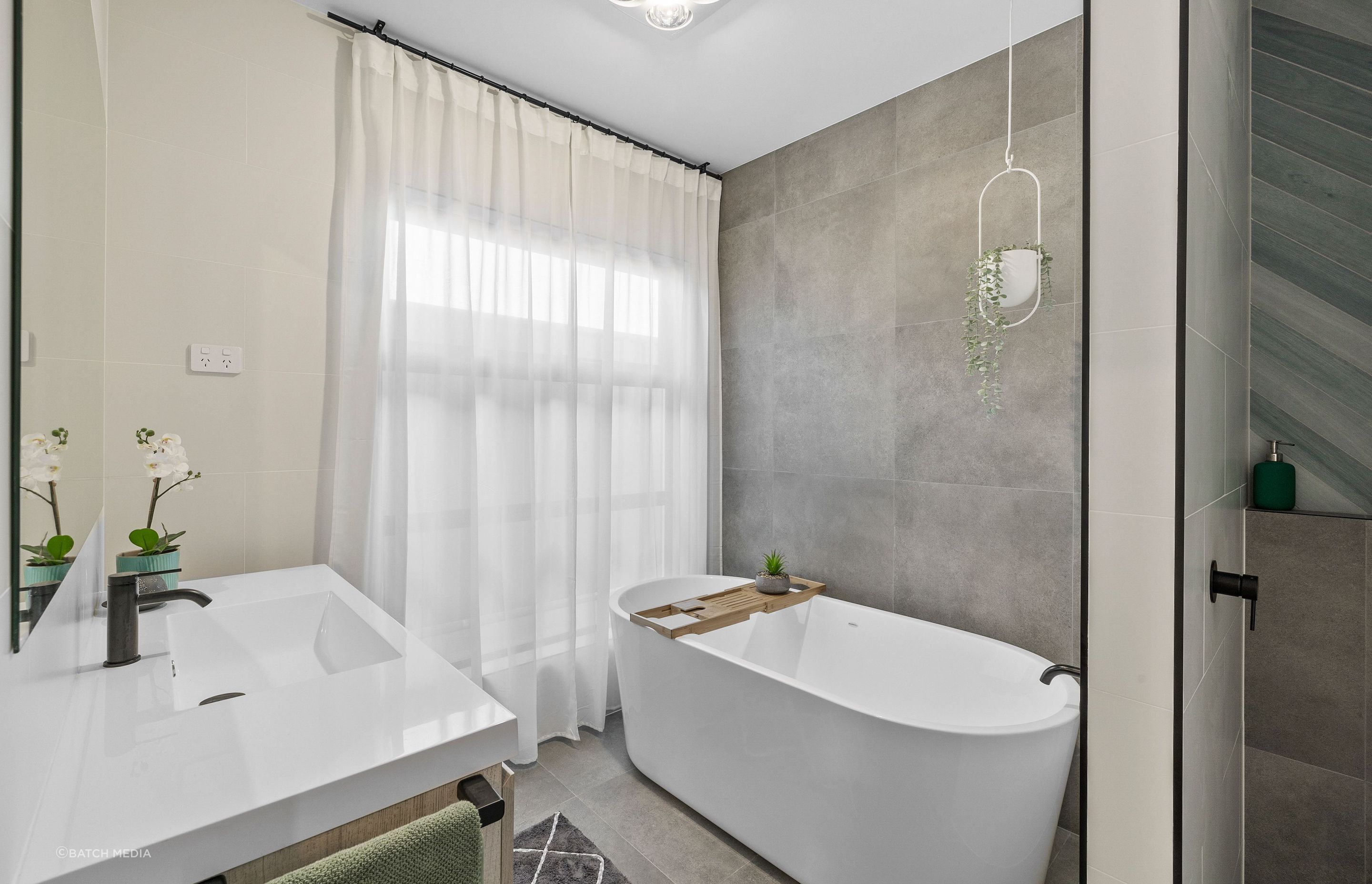 A bathroom space can be designed as a personal sanctuary; this bathroom by Black Line Concepts is elevated through the use of a soft draping curtain and hanging plant.