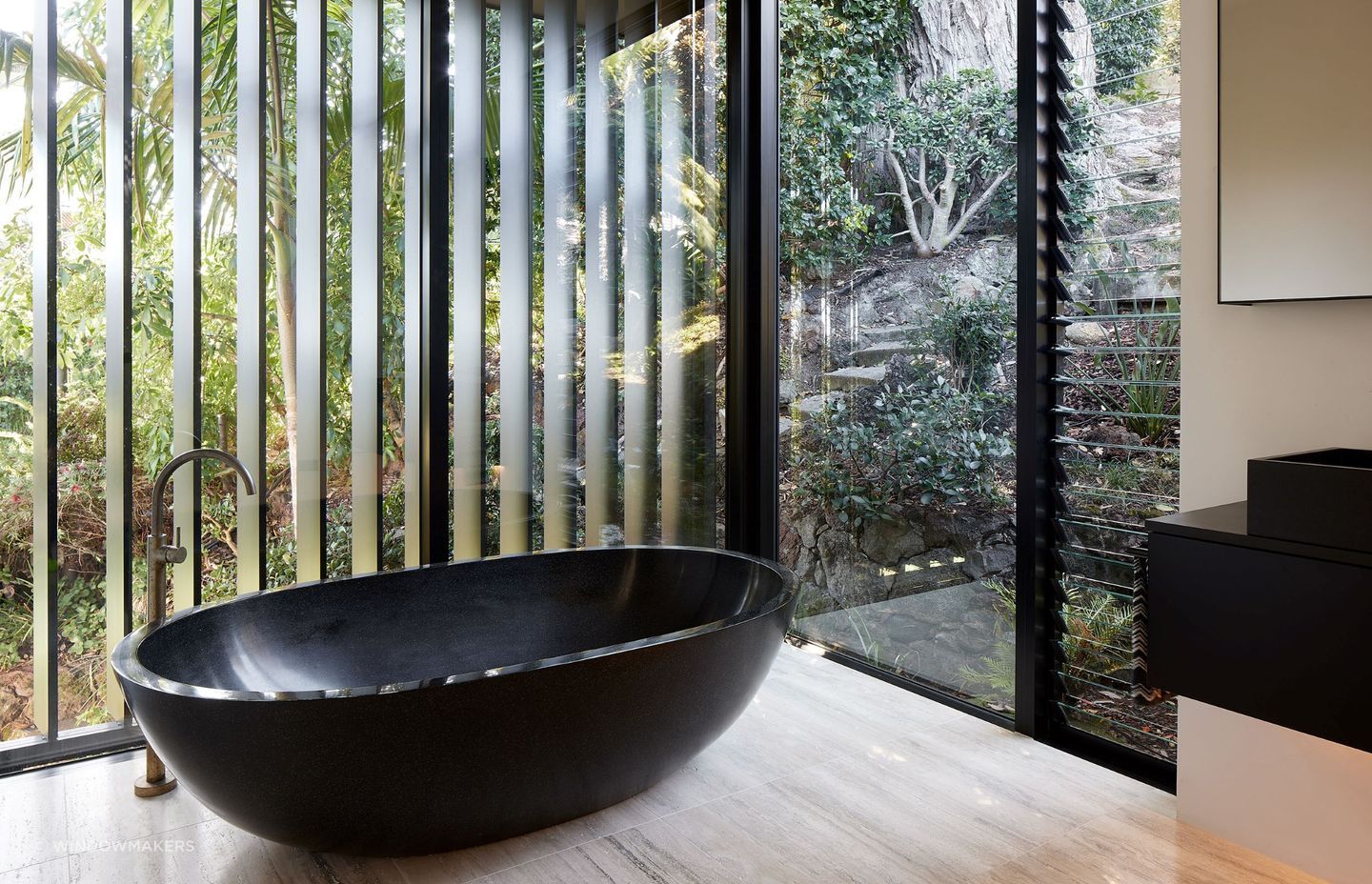 Glass panelling around the statement freestanding tub fully immerses one into the natural surroundings of this Herne Bay home.