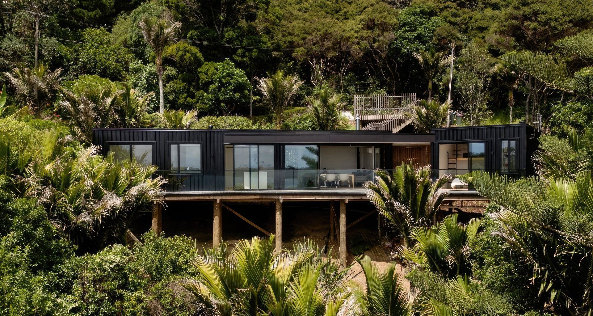 In the picturesque, yet challenging terrain of Waiheke Island, a French couple partnered with Artis Homes to create an affordable yet beautiful home that fits perfectly in its environment. Given the sloping site’s constraints, conventional construction plans like driveways and garages were discarded. Instead, a pragmatic approach was adopted, including a parking platform and walk-down entry stair to preserve the natural surroundings.