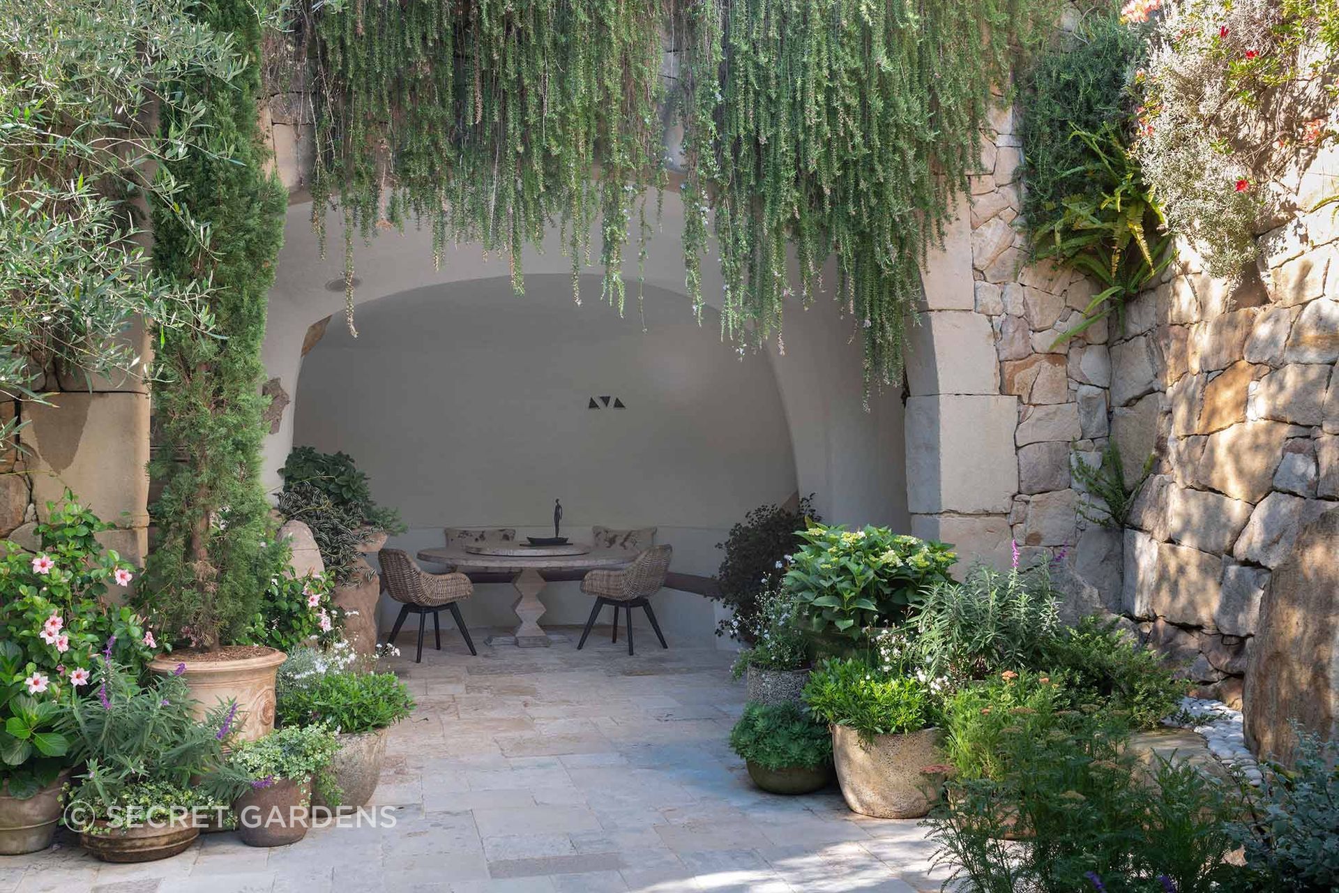 Cascading greenery softens the stone architecture and frames a sheltered dining space, creating the sense of a garden that has evolved organically over time.