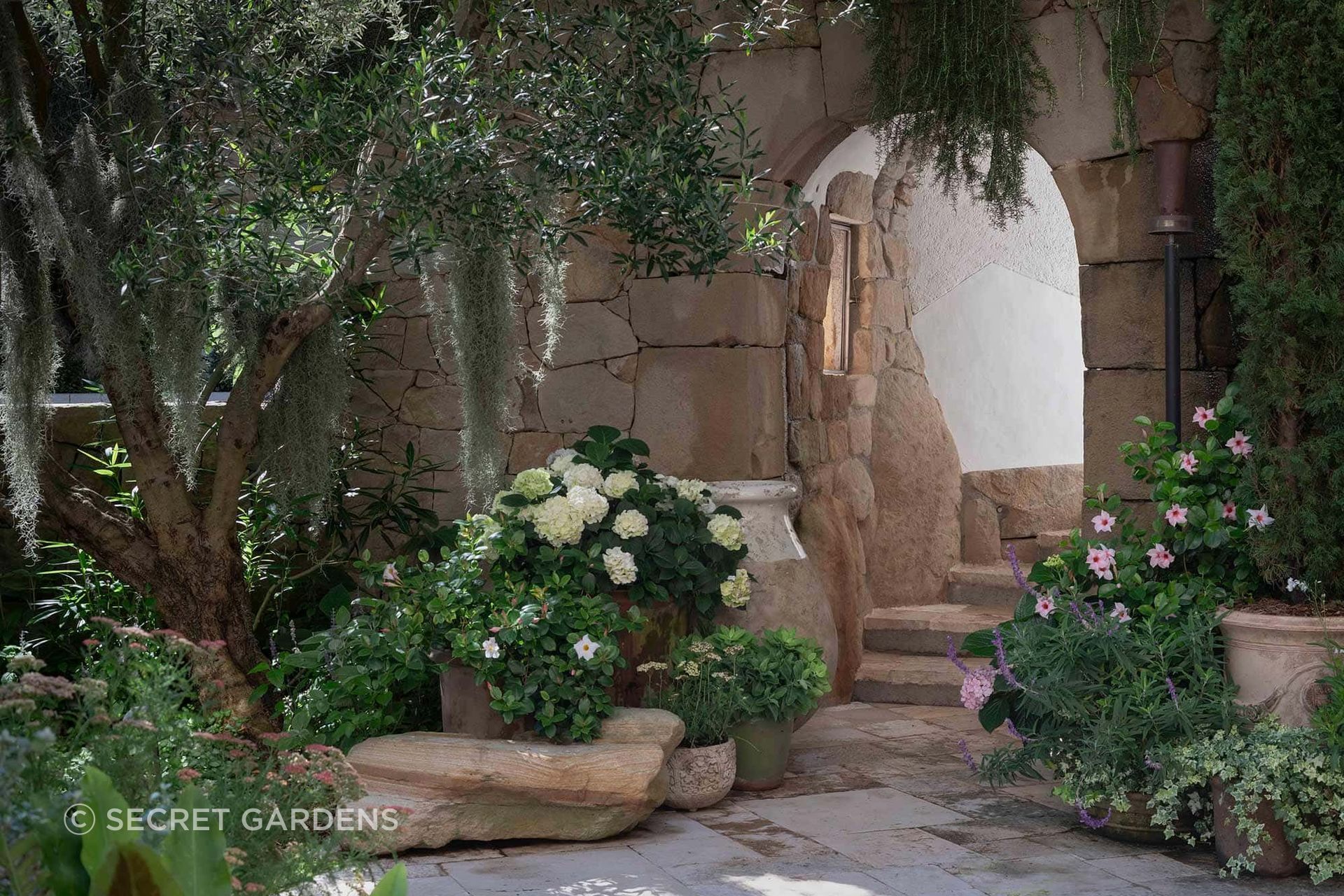Salvaged stone, mature trees and layered planting give the garden an established quality, connecting its newly created spaces with the original landscape.