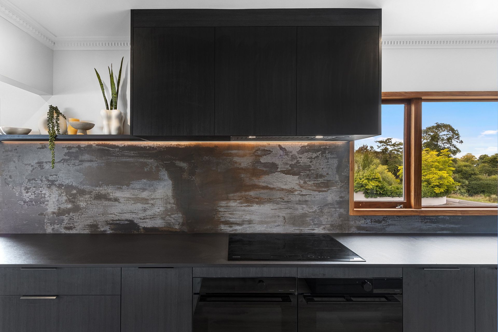 The completed kitchen features dark elements like the Dekton Trilium splashback — chosen for its oxidised finish that mimics the look of reclaimed metal.