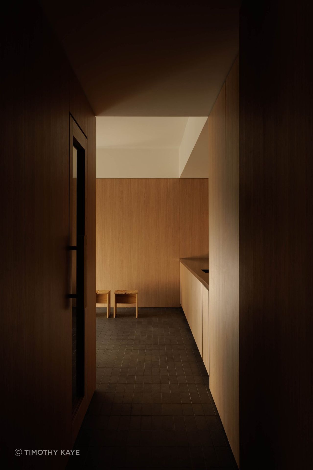 A narrow, timber-lined passage uses shadow, warmth and a restrained material palette to heighten the transition into the bathhouse.