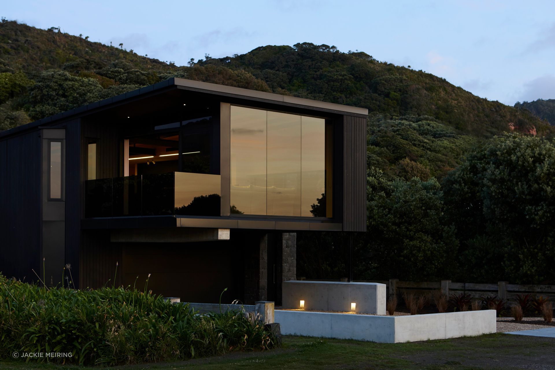 At Piha House, the architecture is shaped by the force of its west coast setting, with a robust material language and cantilevered upper level responding to wind, sand, sea and outlook.