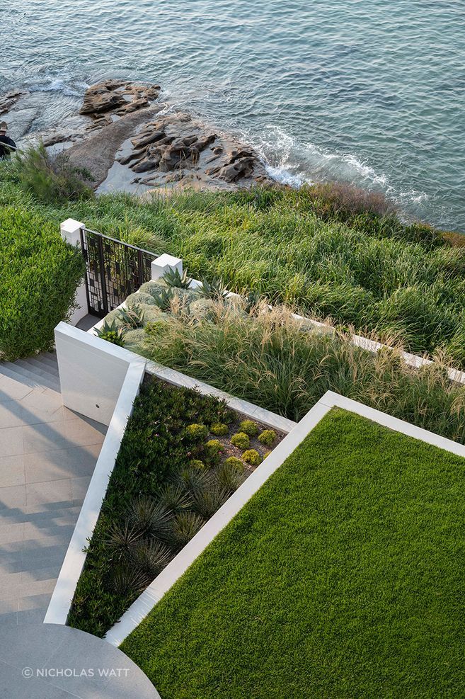 At the water’s edge, structured garden beds balance lawn, layered coastal planting and circulation while preserving the home’s outlook across Port Hacking.