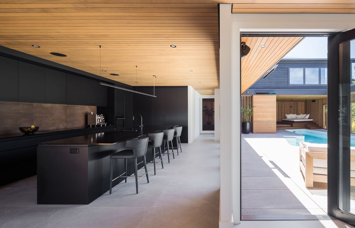 The jet-black kitchen is striking in contrast to the warm-toned cedar and subdued grey tiles.