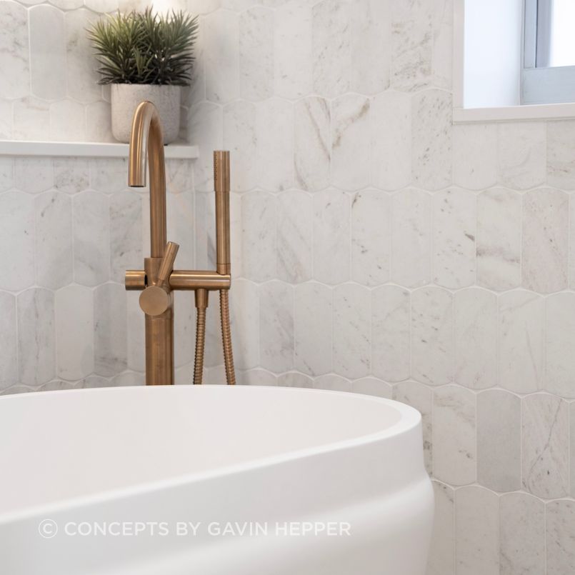 A freestanding bath features alongside natural stone tiles and a bronze floor mounted bathfiller. The elongated wall niche allows for lighting.