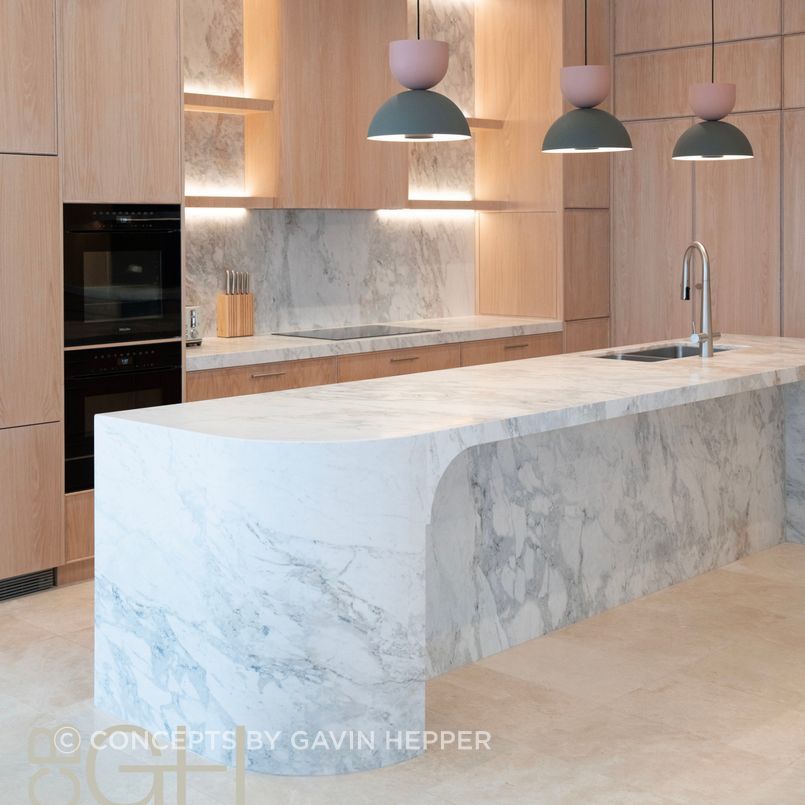 Luxury kitchen renovation featuring warm limewash oak and Celine Dolomite natural stone. Curved elements in the island are echoed in the feautre rangehood