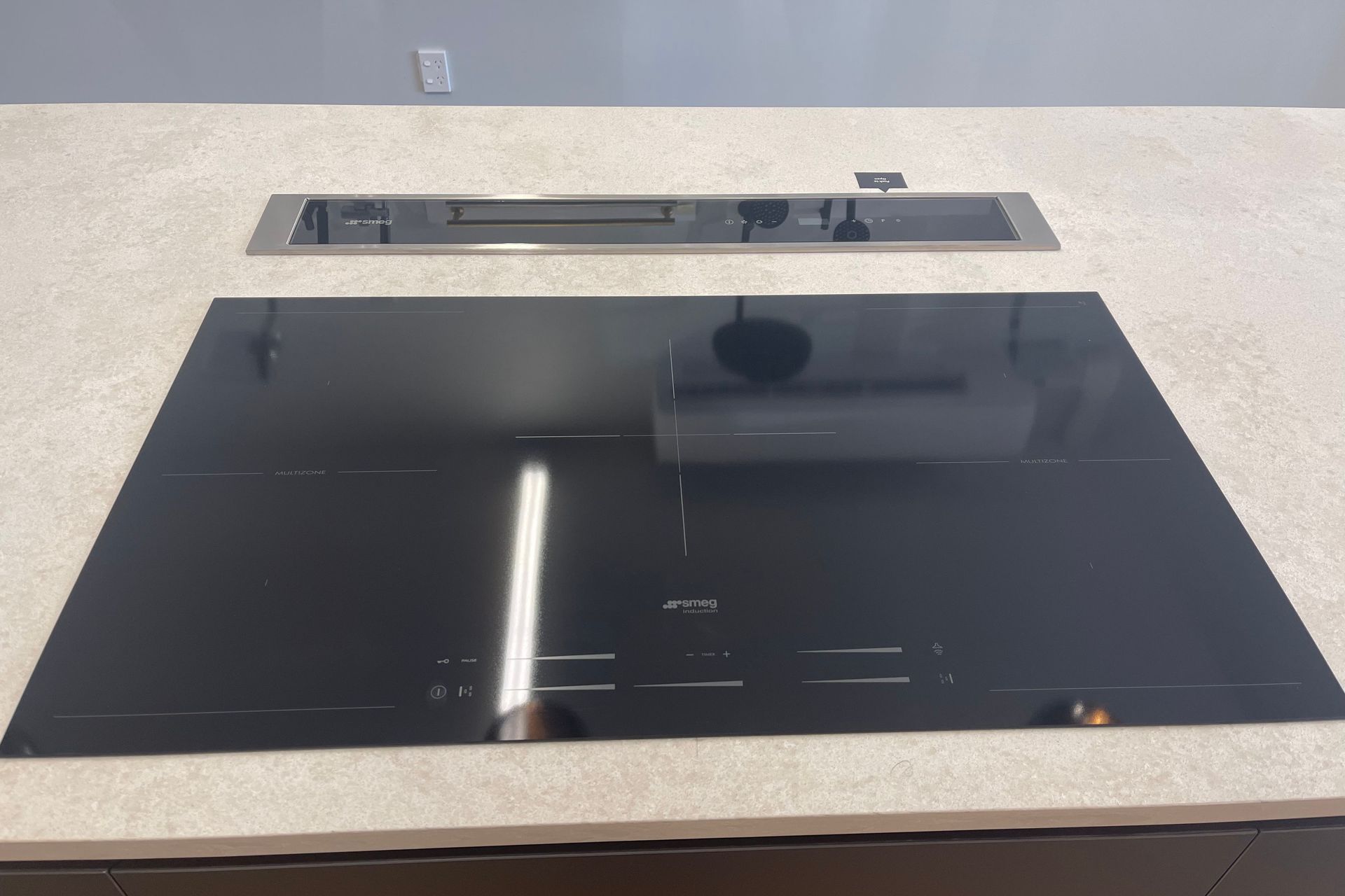 Large induction stovetop from SMEG with a safety feature in our kitchen showroom in Auckland. The downdraft range hood goes back into the benchtop when not in use.