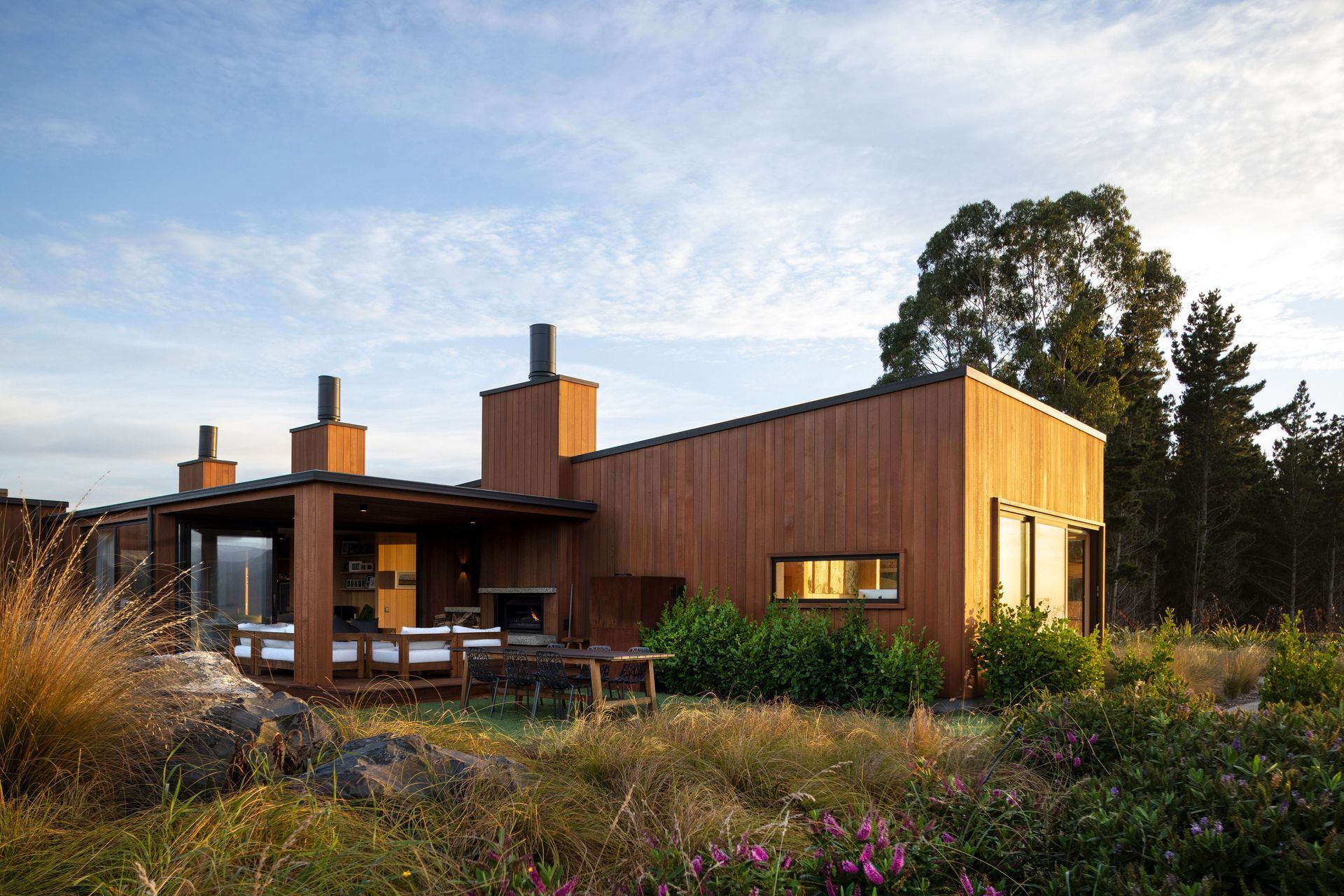 The west-facing side of Coastal Retreat, designed with an outdoor living area that captures the sunset over Blueskin Bay. | Photographer: Graham Warman