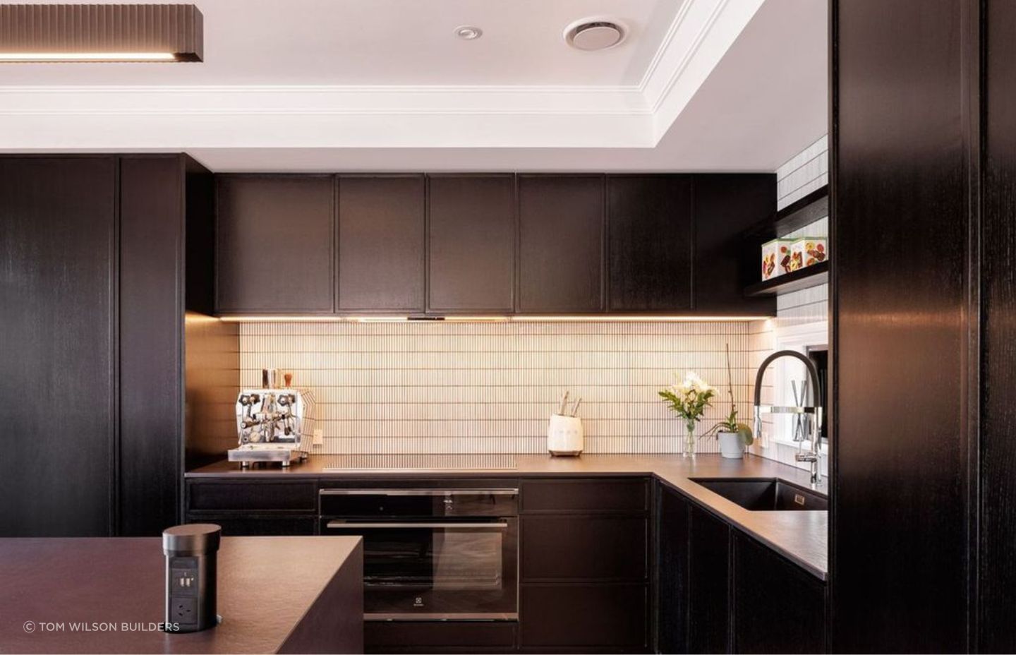 The kitchen, also known as the heart of the home, is designed with dark stained wooden cabinets, sublty lightened with white tiling to add texture and contrast