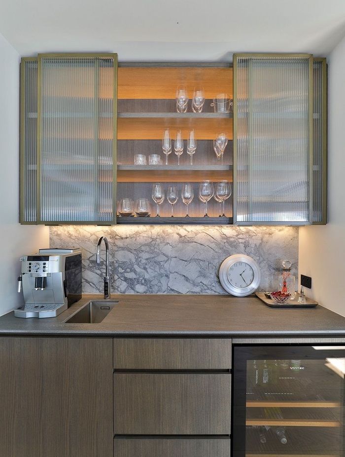 This narrow-reeded glass cabinetry by Hewe Architectural Cabinetry elevates this bar and subtly conceals the items within.