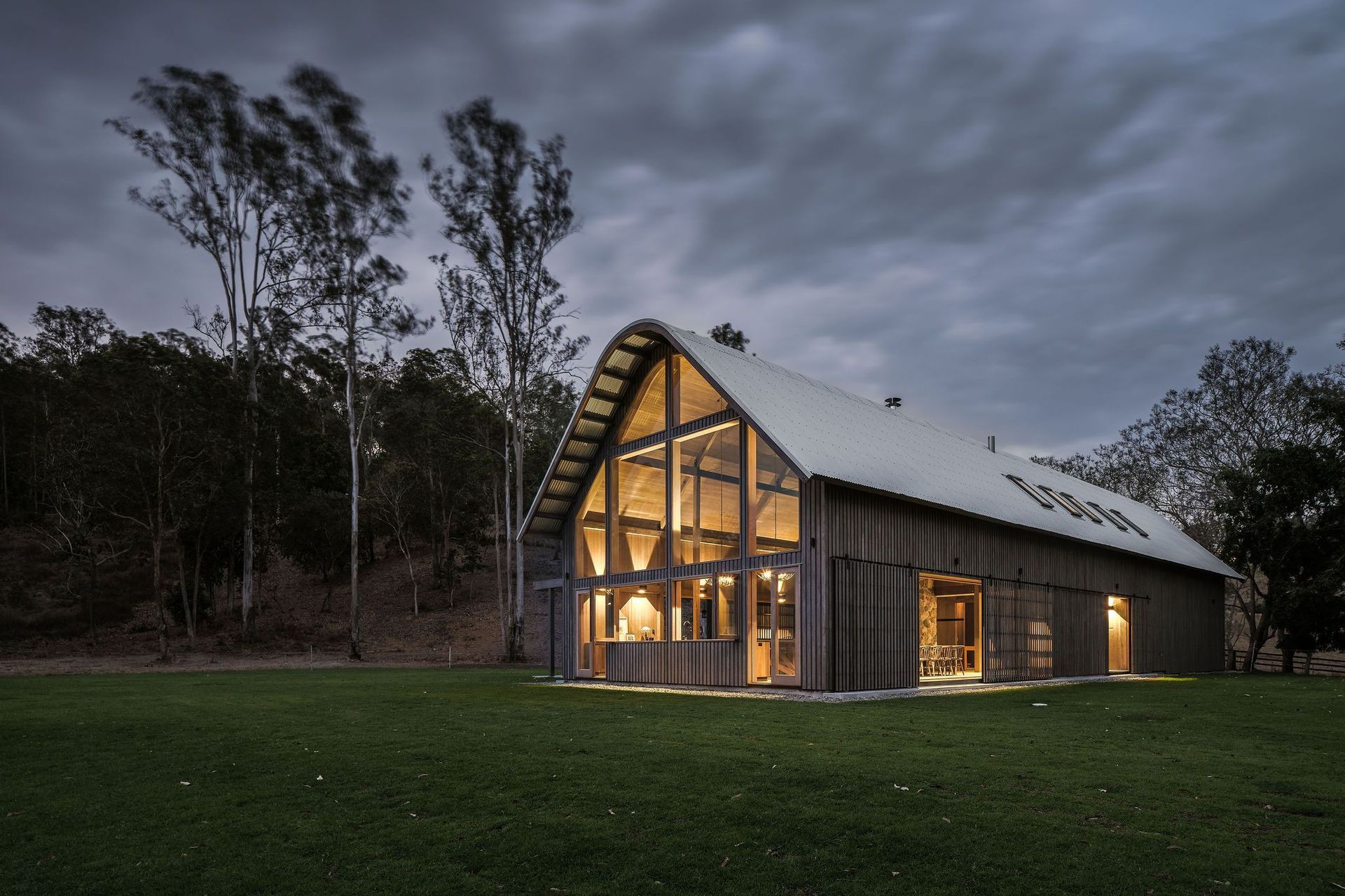 The grand gabled windows of The Barn act as a beacon of warmth against the encroaching wind and evening shadows. Photography: Amy Macpherson Studio.