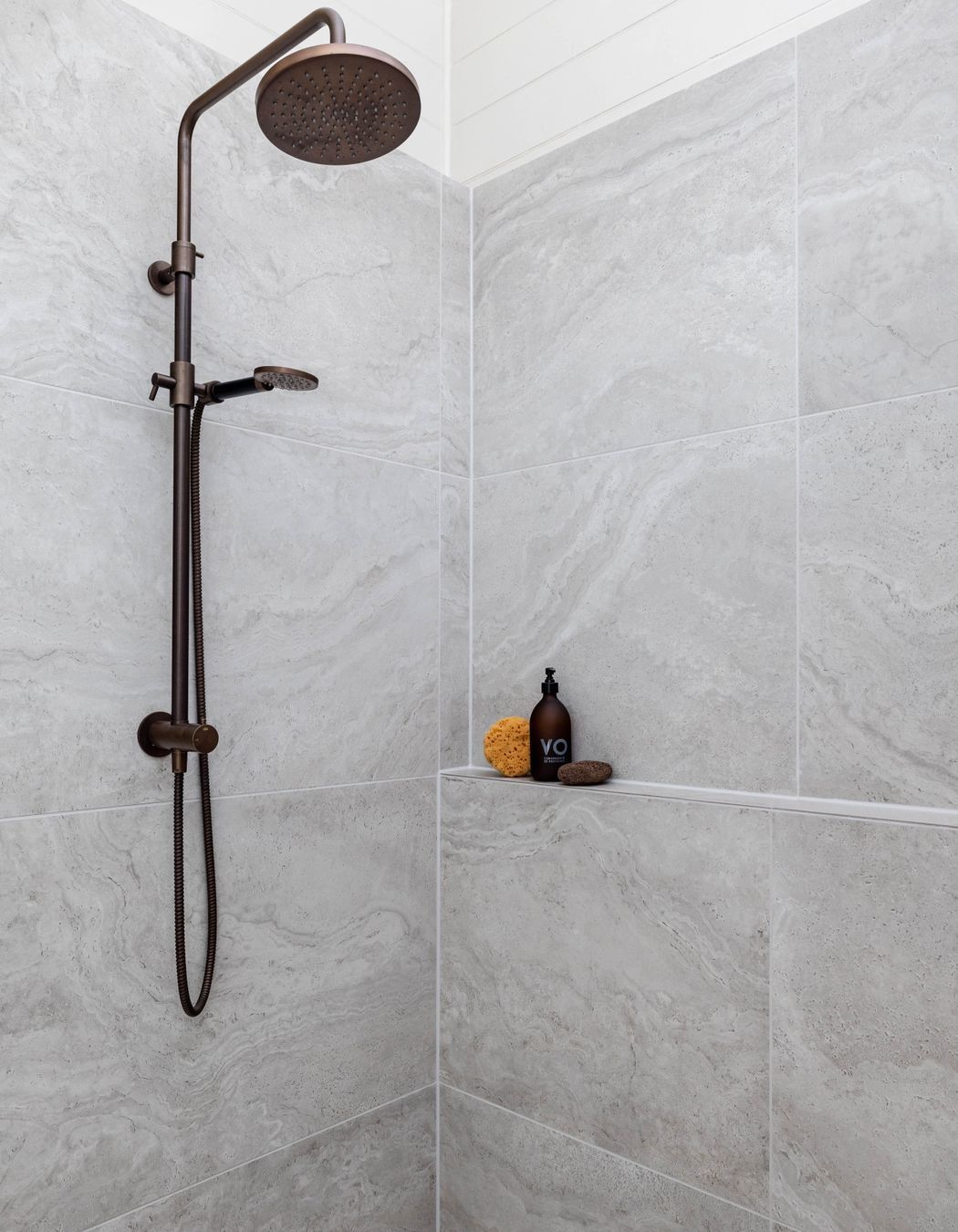 The Plumbline Shower Buddy Column in 'Aged Brass' contrasts with the textural tiles from Quantum.