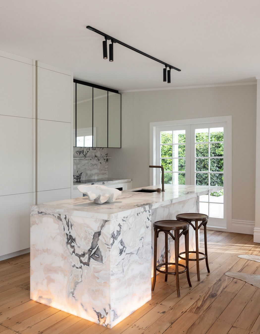 Lighting within the base of the island bench brings warmth to the space. Above, a track light from Coombes + Gabbie provides excellent task lighting for food preparation.