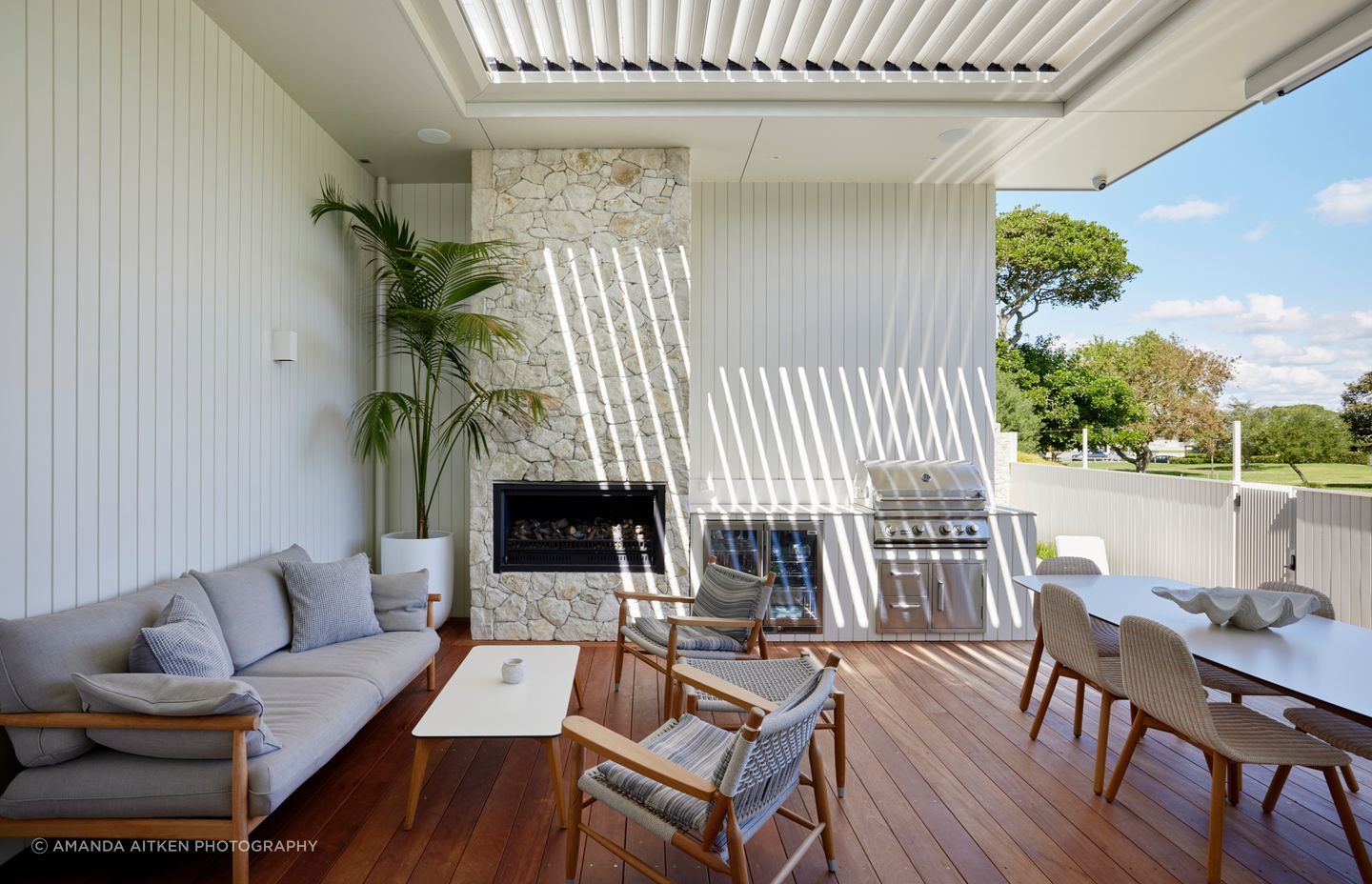 Sliding doors open the kitchen onto an outdoor dining area centred around a limestone fireplace and complete with a built-in fridge, barbecue, and seating.