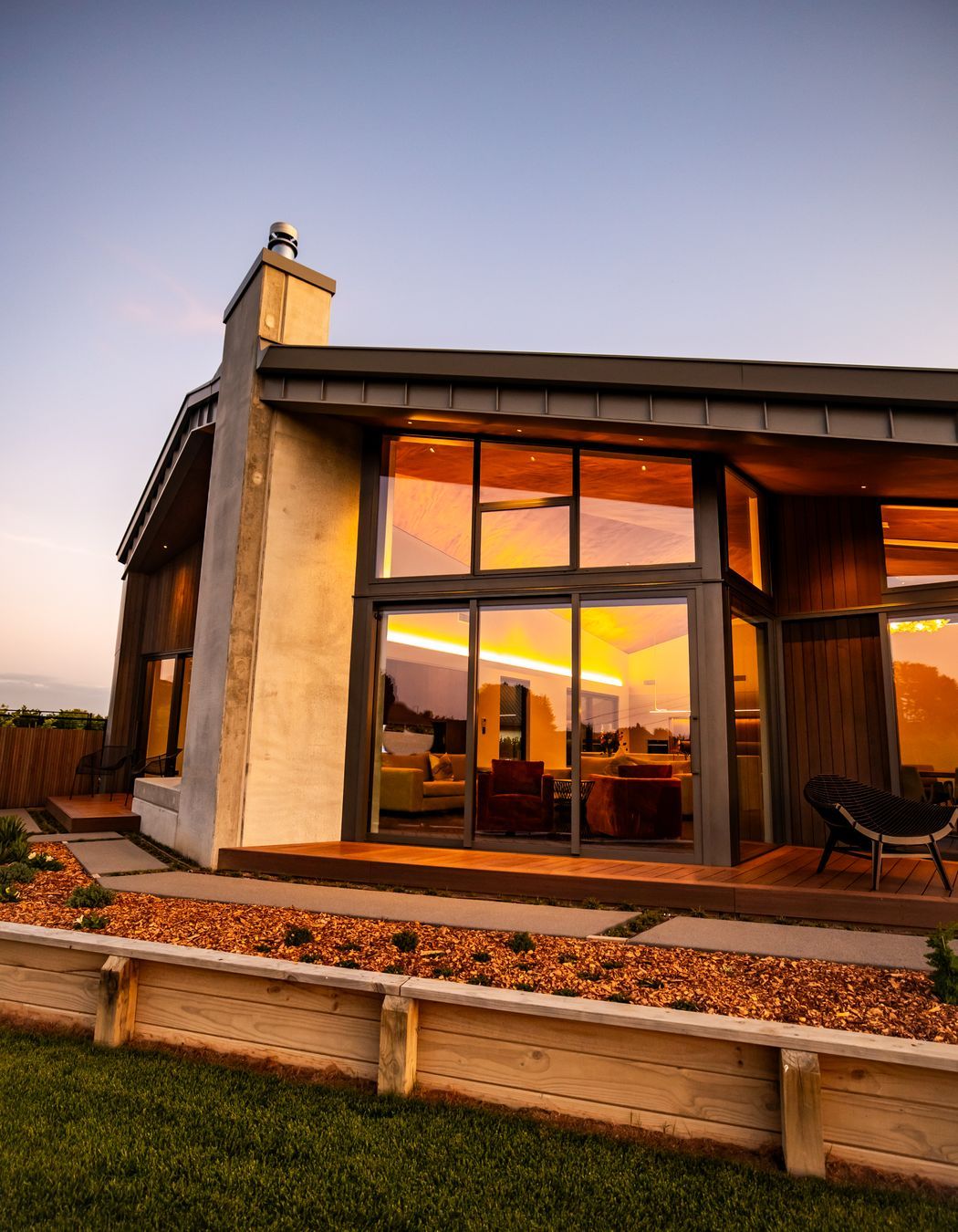 The tray-style roofing tucks down over the home, juxtaposing with the concrete forms and timber decking.