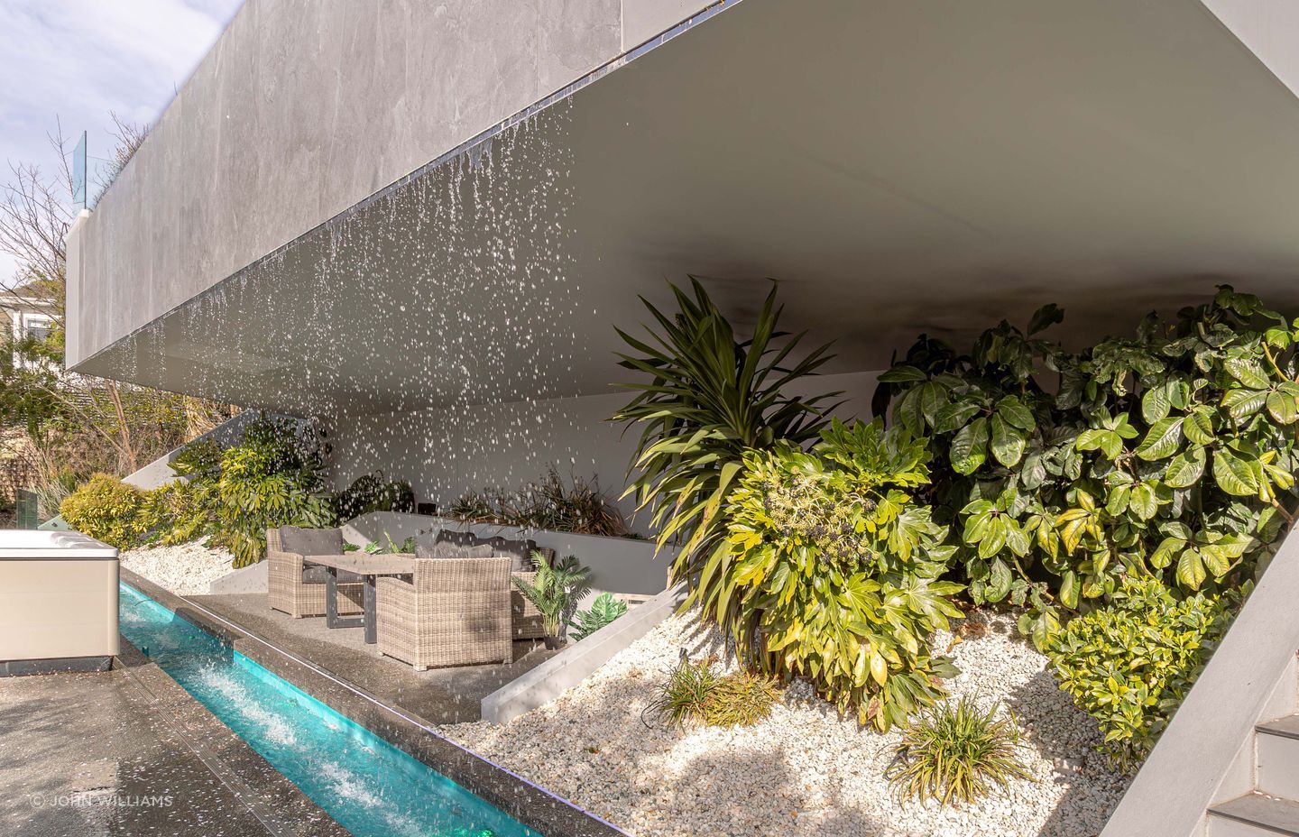 An intimate grotto is recessed behind the waterfall's downpour, complemented by lush foliage.