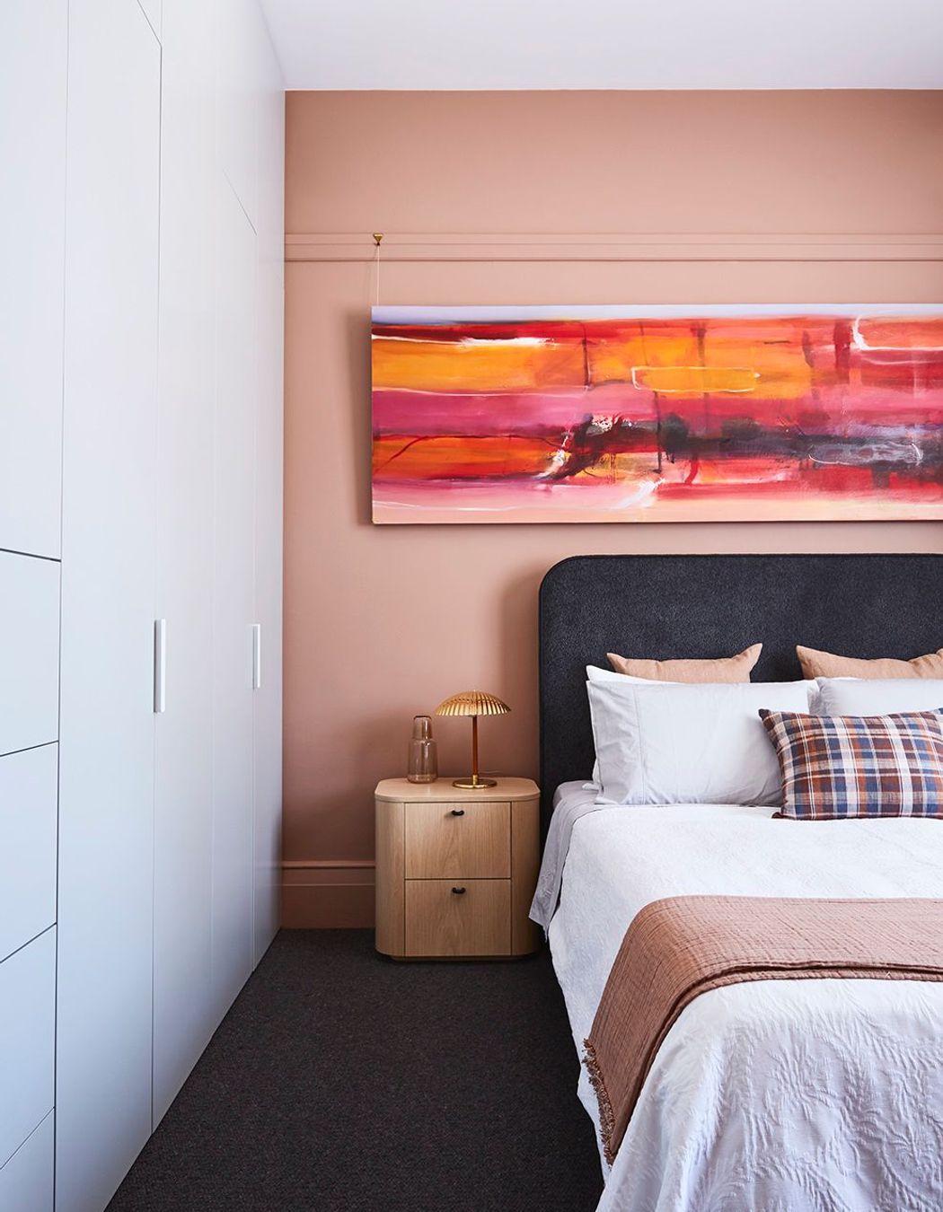 In a bedroom, a pop of pink uplifts and integrates the artwork