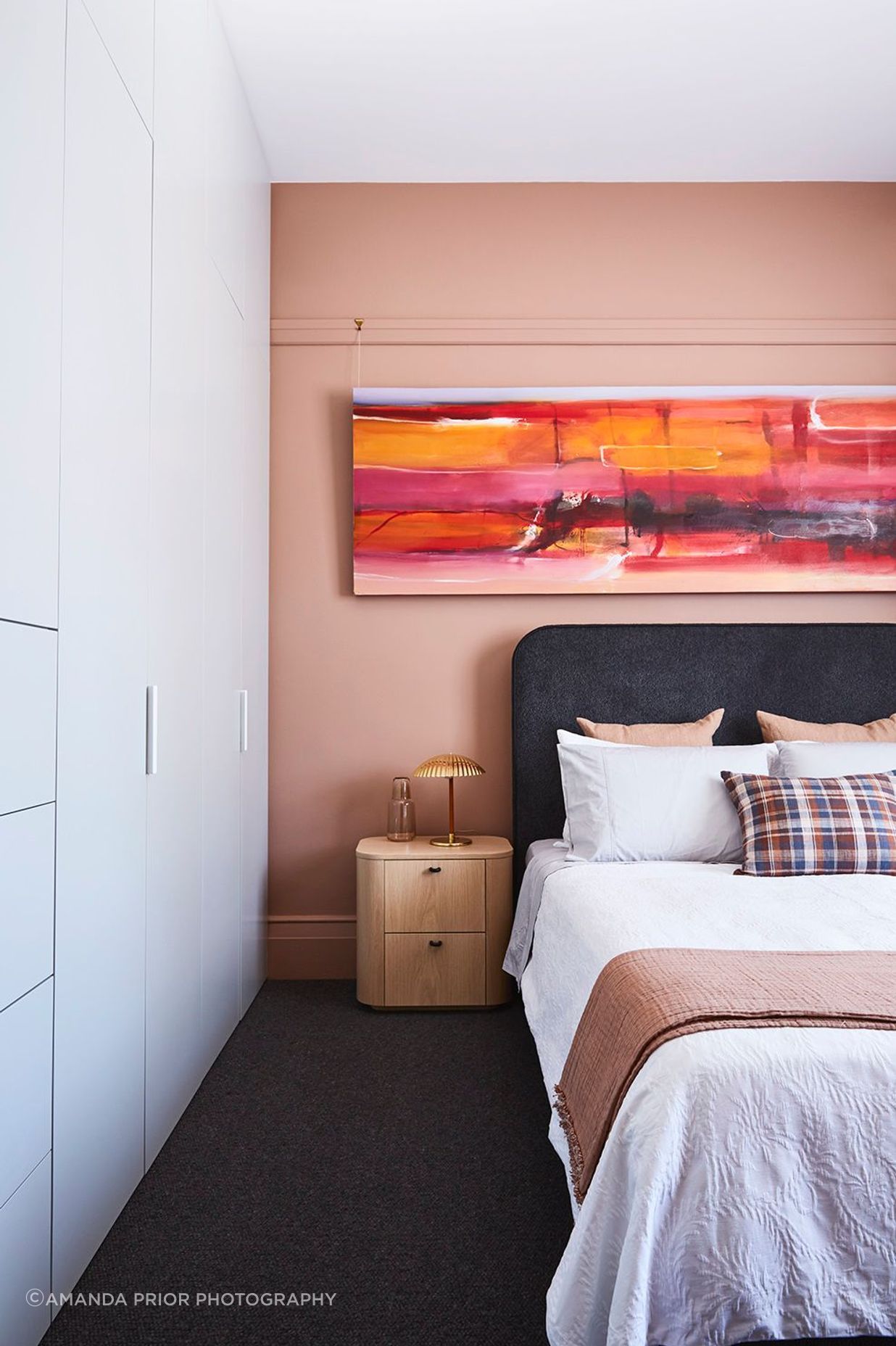 In a bedroom, a pop of pink uplifts and integrates the artwork