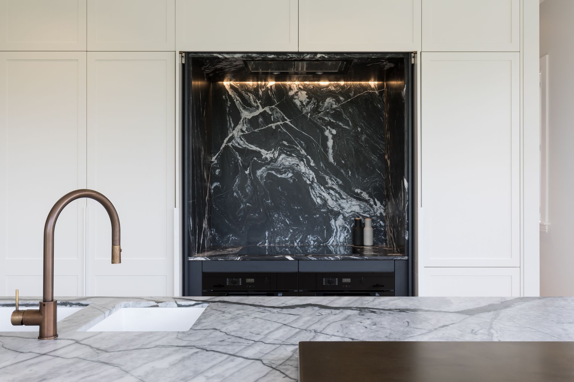 The kitchen in this Auckland family home renovation features Hawa Concepta doors by Häfele in the hob area that pivot and retract into pockets, exposing the bold dark marble counterpoint to the light marble of the island.