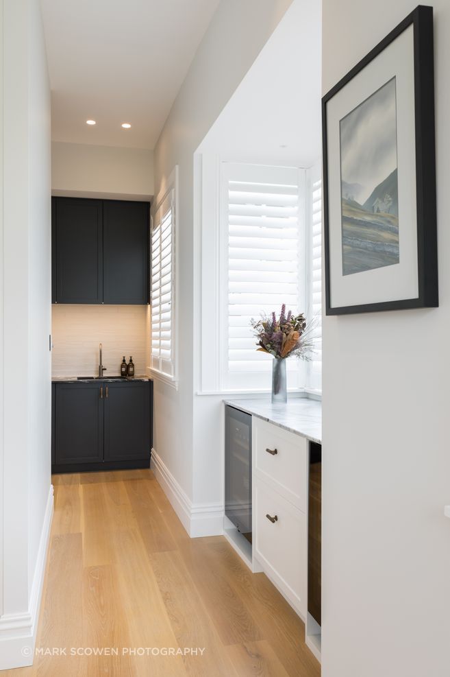 The scullery tucked around a corner hides a second refrigerator. The dark cabinetry in Resene Double Tuna echoes the dark marble used in the kitchen.