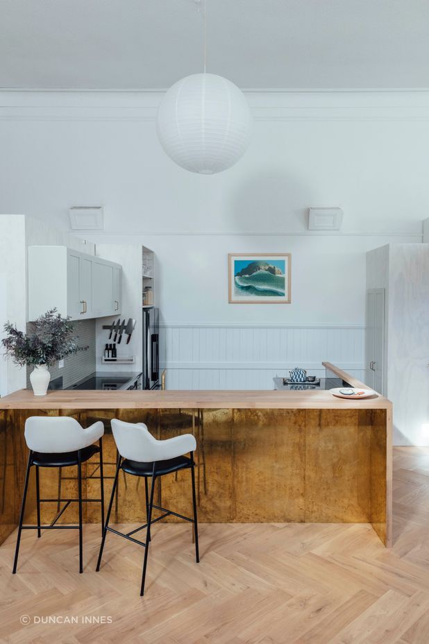 The kitchen features a timber breakfast bar and brass details. 