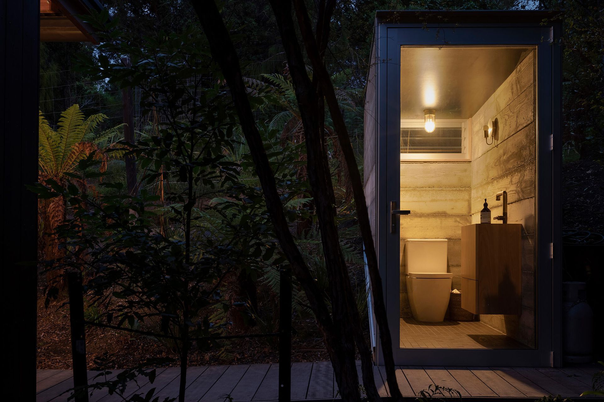 A timber boardwalk leads further uphill to a semi-buried toilet, hunkered into the land with concrete and framed by a fully glazed frontage.