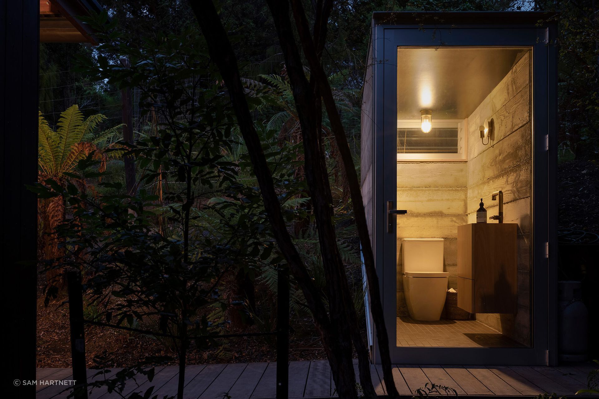 A timber boardwalk leads further uphill to a semi-buried toilet, hunkered into the land with concrete and framed by a fully glazed frontage.