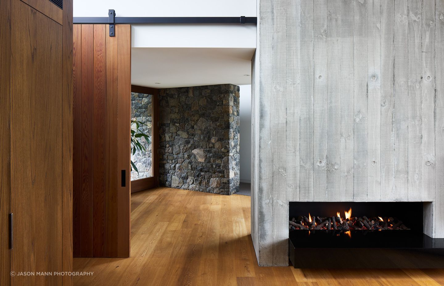 The entrance hall sits at the “knuckle of the two wings”. Its lower ceiling height feels protective, complemented by warmly toned timber. Locally sourced volcanic stone extends from the exterior into the interior, softening the transition whilst firmly rooting the residence in the Port Hills.
