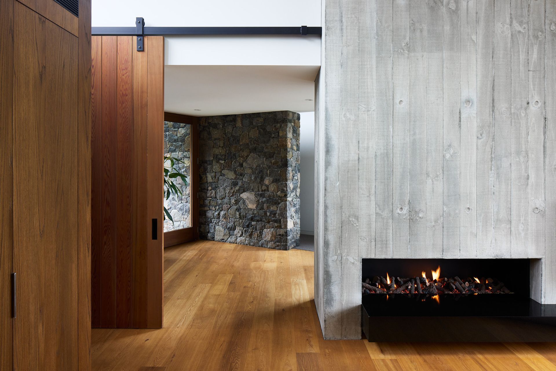 The entrance hall sits at the “knuckle of the two wings”.  Its lower ceiling height feels protective, complemented by warmly toned timber. Locally sourced volcanic stone extends from the exterior into the interior, softening the transition whilst firmly rooting the residence in the Port Hills.