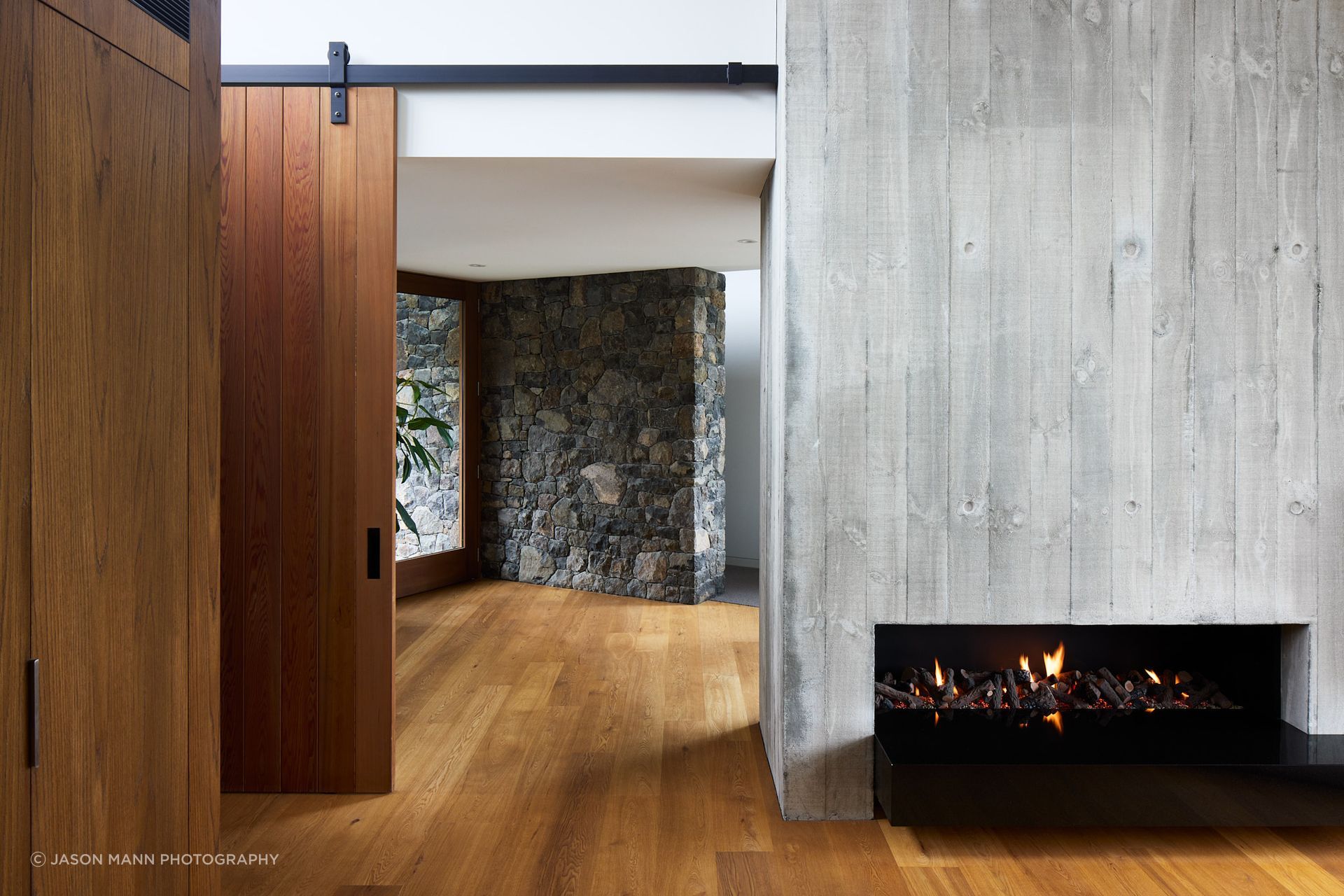 The entrance hall sits at the “knuckle of the two wings”. Its lower ceiling height feels protective, complemented by warmly toned timber. Locally sourced volcanic stone extends from the exterior into the interior, softening the transition whilst firmly rooting the residence in the Port Hills.