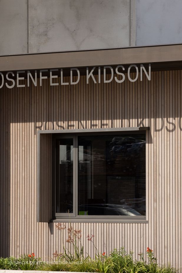 The asymmetric window shroud is for sun control. The tilt slab concrete wall of the factory can be seen behind the building.