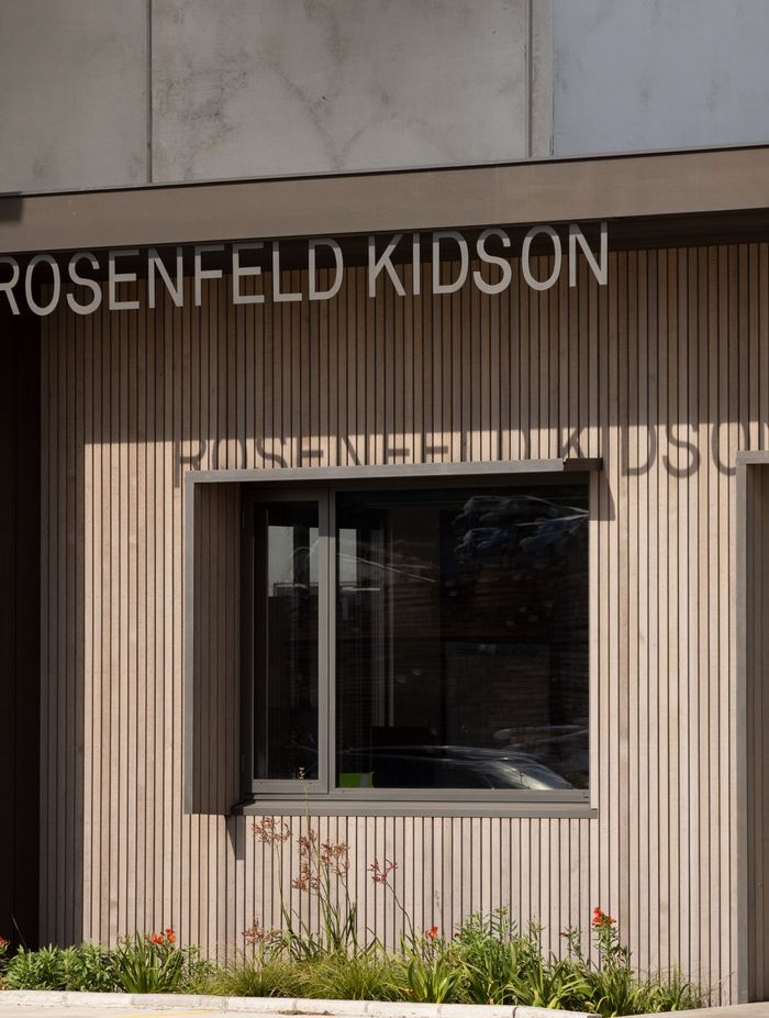The asymmetric window shroud is for sun control. The tilt slab concrete wall of the factory can be seen behind the building.
