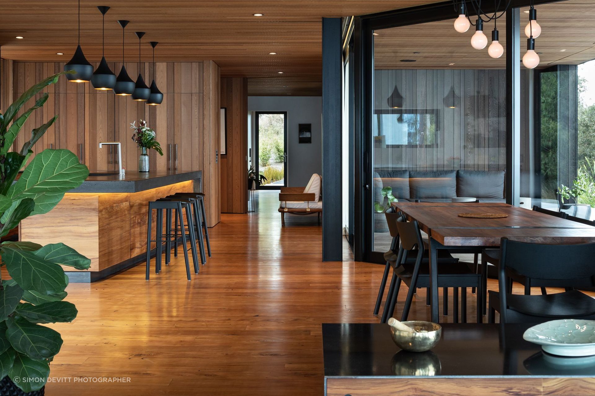 The cedar ceiling and recycled rimu flooring mirror each other, giving way to black accents of the aluminium joinery, exposed concrete, and other finer details.