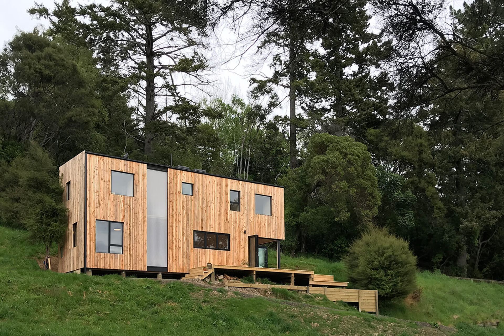 The dramatic exterior of the Akaroa Bach by Makers of Architecture in amongst manuka bush and rural farmland