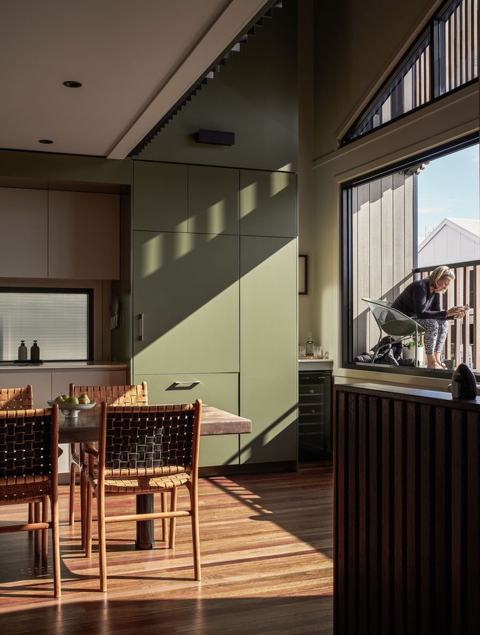 The palette features soft hues of sage and pale greens paired with natural timbers. To the right of the kitchen, a small balcony overlooks the street, capturing the morning and midday sun as it’s filtered through the timber batten screen.