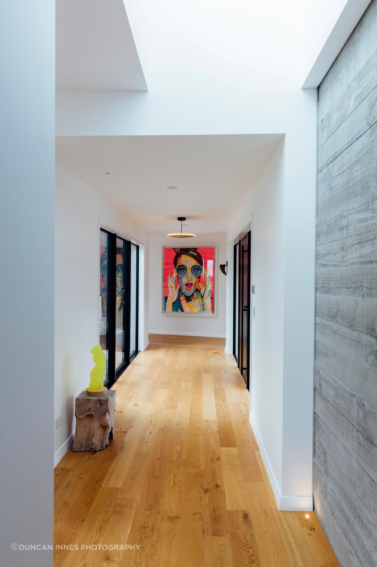 The long run of hallway, with concrete tilt panels on display and an artwork by the homeowners. Afternoon light enters through the skylights and washes down the walls, says Brendon.