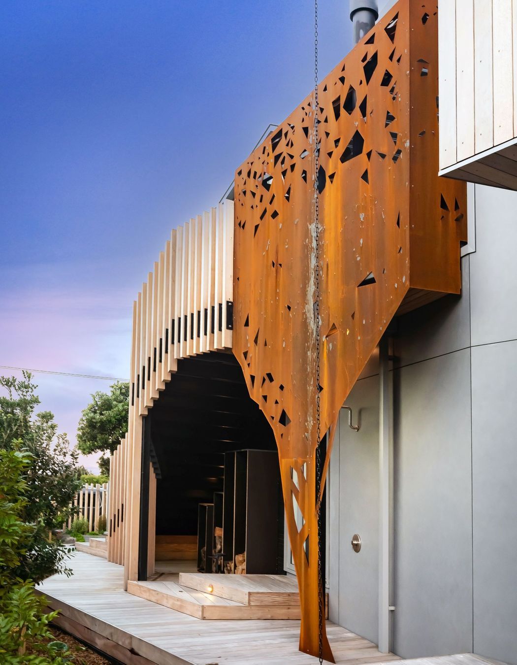 Wrapping around the outdoor fireplace, corten steel has been formed to mimic the silhouette of a pōhutukawa tree across the road from the house.