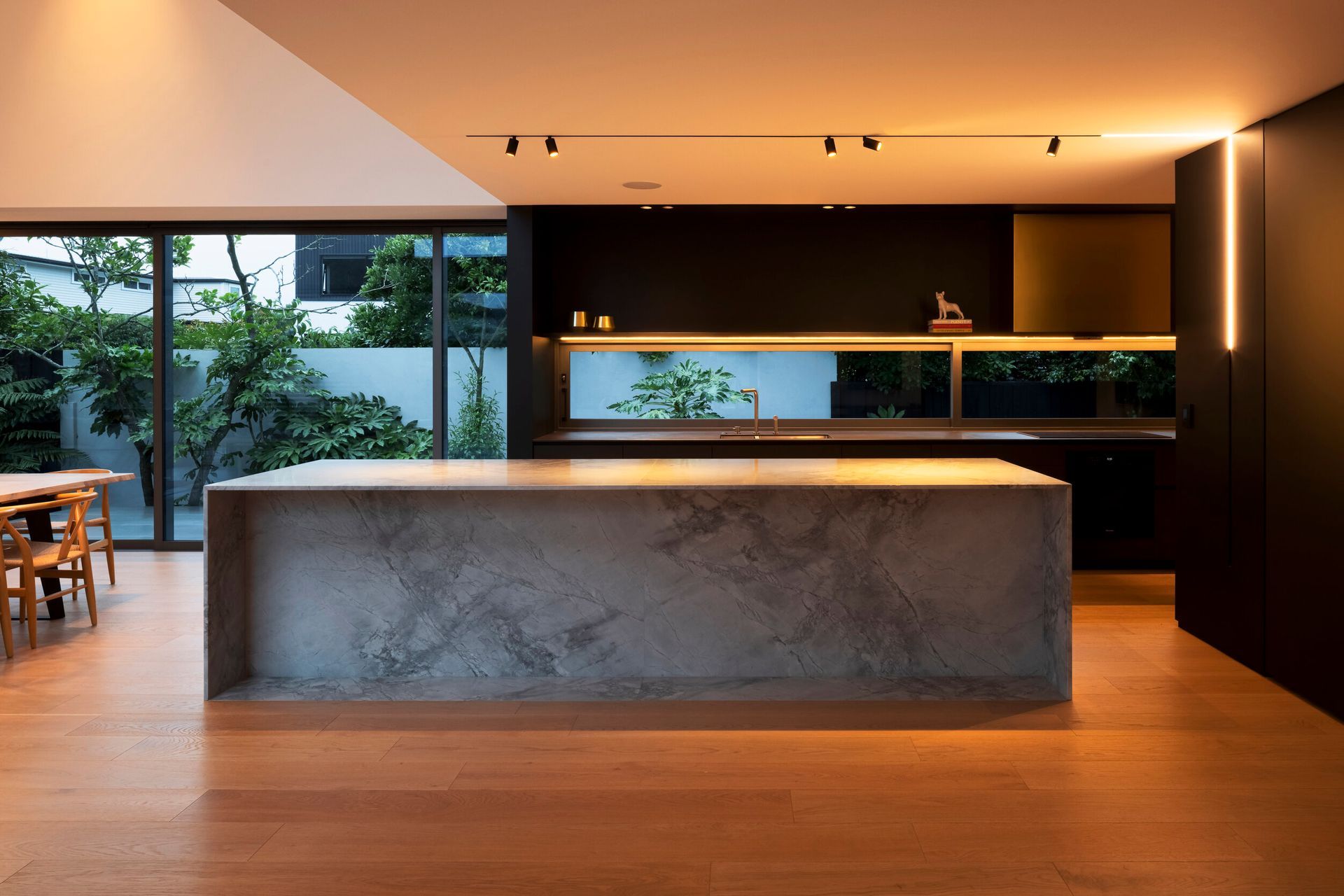 The kitchen is centrally positioned in the flattened 'T' shape arrangement, spilling into two living areas with distinct spatial experiences.